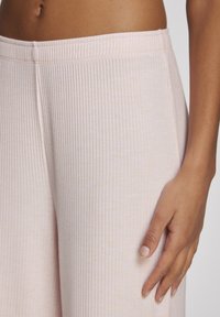 Inimene, kes kannab heleroosat soonikpükse elastse vöökohaga, käsi õrnalt reiel.