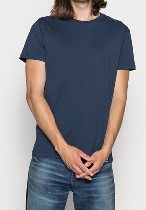 T-shirt a maniche corte blu navy realizzata in tessuto morbido, con colletto rotondo e vestibilità rilassata, abbinata a jeans in denim azzurro chiaro.