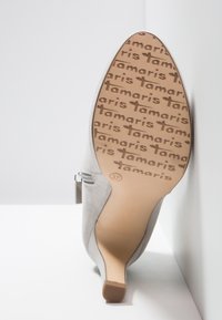 Chaussure à talon haut en daim gris avec bout pointu, fermeture éclair sur le côté, et semelle embossée du logo "Tamaris" répété ainsi que la taille 37.