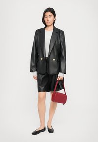 Svart faux skin blazer med gullknapper, kombinert med en grå genser, svarte faux skin shorts og en liten rød veske. Svarte leiligheter.