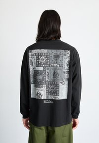 Czarna koszula z długim rękawem z dużym szarym nadrukiem graficznym na plecach, przedstawiającym różne wzory i obrazki oraz logo na dole.