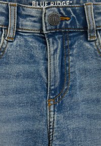 Hellblaue Jeans aus Denim mit einem bronzefarbenen Knopf, kupferfarbenen Nähten und einem klassischen Design mit fünf Taschen. Verfügt über eine ausgebleichte Textur.