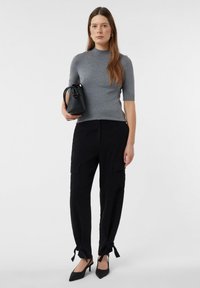 Szary krótki sweter z krótkim rękawem w połączeniu z czarnymi spodniami cargo z bocznymi kieszeniami i detalami w postaci sznureczków na dolnej krawędzi, dopełnione czarnymi szpilkami.