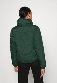 Giacca a vento verde con colletto alto, caratterizzata da un motivo a zigzag sul corpo, polsini elasticizzati e vestibilità corta. Tessuto testurizzato.