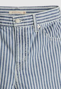 Höga, vida shorts med vertikala blå och vita ränder. Har en knappstängning, framficka och mjuk denimtextur. Storleksetikett synlig.