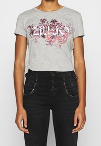 Camiseta gris con gráfico floral en rosa y morado, de manga corta, con cuello redondo, combinada con jeans negros de cintura alta con detalles de tachuelas.