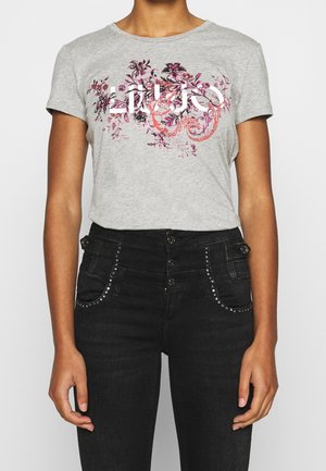 Grijze t-shirt met een bloemenprint in roze en paars, korte mouwen, ronde halslijn, gecombineerd met hoge zwarte spijkerbroek met studs.