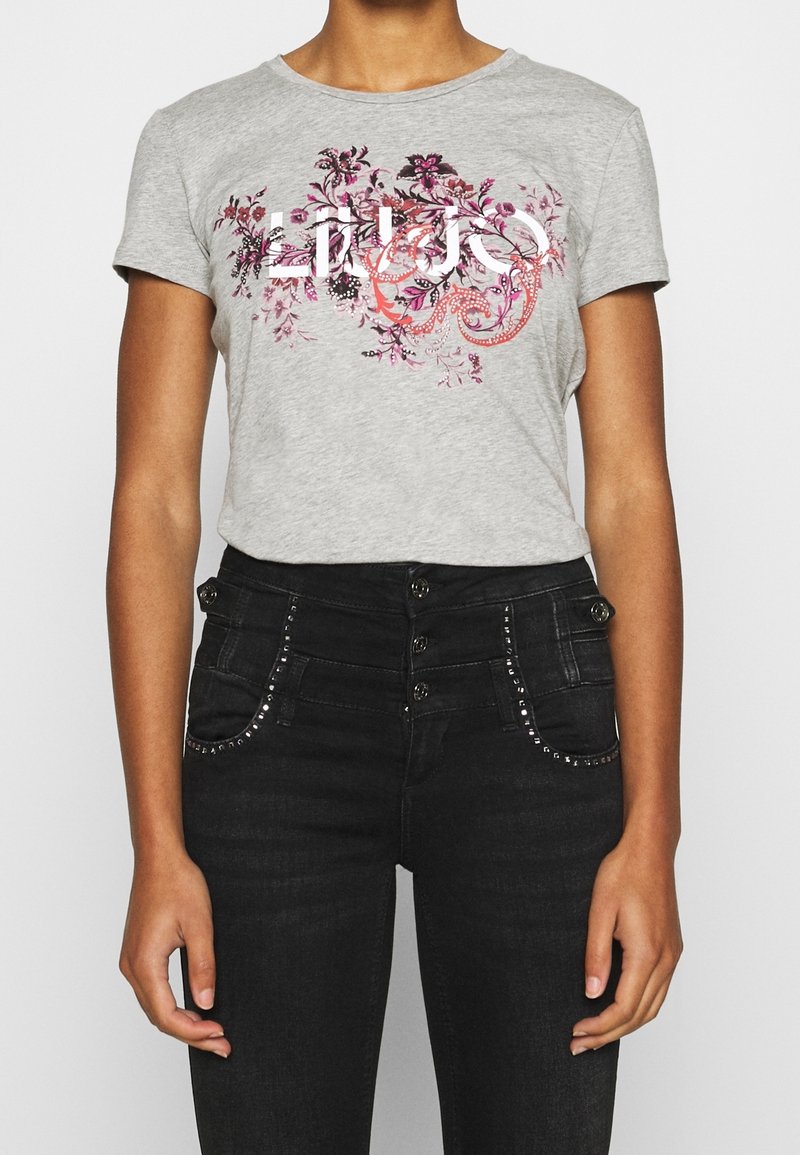 Camiseta gris con gráfico floral en rosa y morado, de manga corta, con cuello redondo, combinada con jeans negros de cintura alta con detalles de tachuelas.