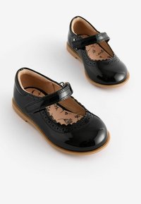 Svarta lackläders Mary Jane-skor med rundad tå, scalloped kant och vävband. Bruna gummisulor med blommönstrade insoles.