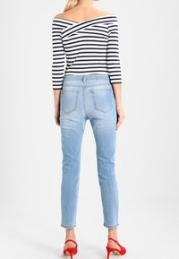 Top de hombros descubiertos a rayas en azul marino y blanco. Jeans de tiro alto de color azul claro con corte ajustado. Sandalias de tacón alto y tiras rojas.