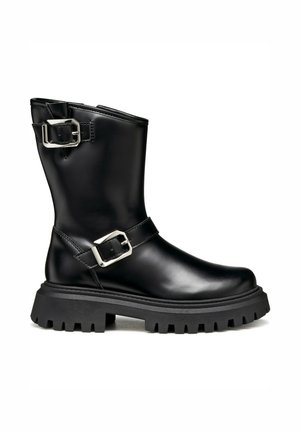 Botte cheville en cuir noir avec deux boucles en argent, une semelle épaisse texturée et un bout légèrement arrondi. Présente une finition lisse et un design robuste.
