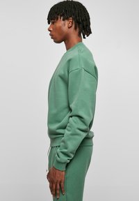Felpa verde con collo a giro, polsini e orlo a costine. Realizzata in un materiale morbido, presenta una vestibilità rilassata e un design minimale.