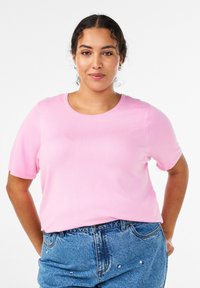 Gaiši rozā īss piedurkņu T-krekls ar apaļu kakla izgriezumu, izgatavots no gludas auduma. Valdīts kopā ar džinsa šortiem ar dekoratīvām detaļām.