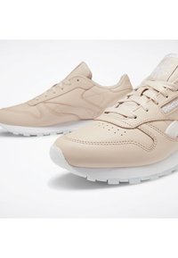 Paire de baskets Reebok beiges avec semelles blanches, coutures détaillées et lacets sur un fond blanc uni.