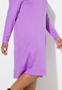 Fialové šaty s dlouhým rukávem vyrobené z měkké, lehké látky. Mají volný střih a přímočiary střih, končící nad kolenem.