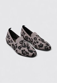 Zapatos de slip-on negros y beige con un material de punto texturizado, que presentan un diseño de estampado de leopardo y una forma de punta afilada.