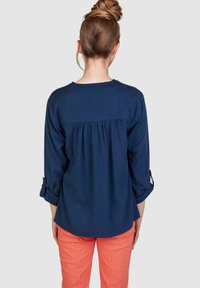 Marineblaue Bluse mit einem gerafften Rückendesign, langen, hochgerollten Ärmeln und einer lockeren Passform, kombiniert mit korallenfarbenen Hosen. Schlichte Textur.