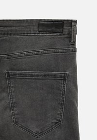 Back pocket area of dark gray denim jeans with visible stitching and a black leather brand patch on the waistband.