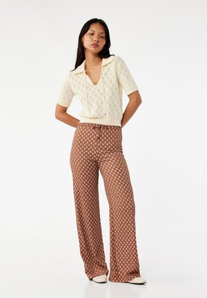 Knit crème trui met korte mouwen en openwerkdesign met een v-hals. Loszittende bruine broek met een patroon, wijde pijpen en een koord in de taille.