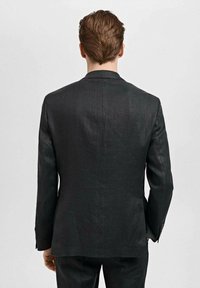 Schwarzer maßgeschneiderter Blazer mit einem einzigen Schlitz, strukturierten Schultern und langen Ärmeln. Besitzt eine subtile Textur und ein minimalistisches Design.