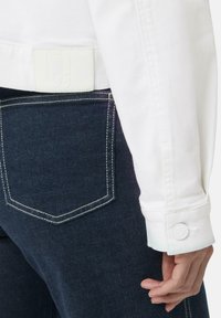 Witte denimjas met een gestructureerde pasvorm, voorzien van grote manchetten en een geprofileerde patch op de achterste tailleband. Donkerblauwe jeans met witte stiksels.
