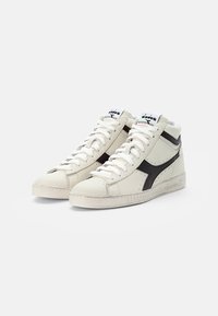 Baskets montantes blanches avec des accents noirs, fabriquées en cuir, dotées d'une semelle texturée, d'un design à lacets et d'un logo sur la languette.