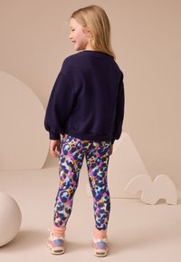 Navy sweatshirt with puffed sleeves, paired with colorful, patterned leggings featuring purple, blue, and yellow spots. White sneakers with accents.
