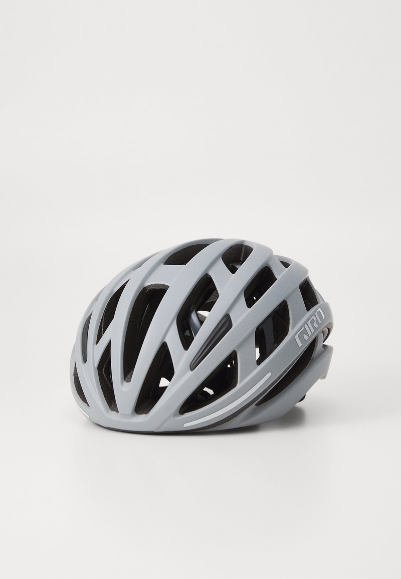 Šedá cyklistická helma s aerodynamickým designem, která má několik ventilací, hladký matný povrch a logo na boku pro identifikaci značky.