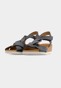 Sandales en cuir noir avec des brides croisées, fermetures Velcro à la cheville, semelles intérieures rembourrées couleur beige, semelles blanches et petits talons compensés en liège.