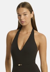 Czarny kostium kąpielowy na halter z głębokim dekoltem w kształcie V i złotym paskiem akcentującym w talii. Gładki, elastyczny materiał.