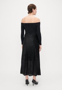 Sort off-shoulder top parret med en sort plisseret nederdel, pyntet med små glitrende accenter, som har en glat tekstur og gulvlængde.