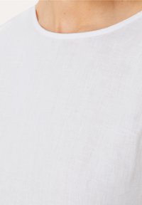 Top in lino bianco con scollatura rotonda, realizzato in un tessuto leggero e leggermente testurizzato. Design pulito e semplice. Nessun motivo o dettaglio visibile.