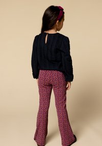 Donkerblauw textuur langemouwen top met een keyhole achterkant, gecombineerd met paarse flared broeken met een kleurrijk abstract patroon.