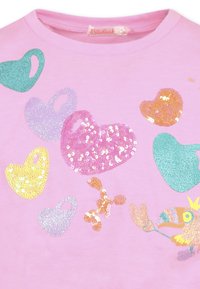 T-shirt rose avec des cœurs en sequins colorés de différentes tailles et couleurs, accompagnée d'un motif de dessin animé d'oiseaux en bas.