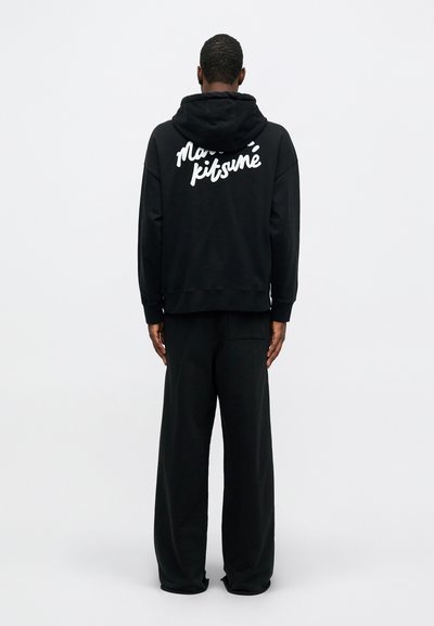 Hanorac negru cu glugă, având text alb "Maison Kitsuné" pe spate, asortat cu pantaloni negri cu o croială lejeră. Material moale, design relaxat.