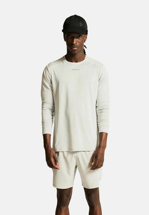 Hellgraues Langarmshirt mit Rundhalsausschnitt und eng anliegenden Ärmeln, kombiniert mit passenden Shorts. Eine schwarze Kappe rundet das Outfit ab.