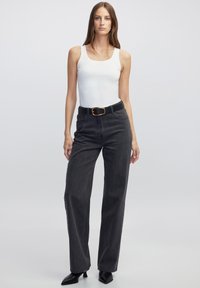 Zwarte high-waisted jeans met een rechte pijp, gecombineerd met een witte mouwloze top en een zwarte riem met een gouden gesp.