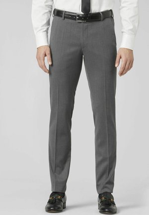 Man wearing gray formal trousers, black leather belt, white shirt, black tie, and black loafers with tassels, standing against plain background.