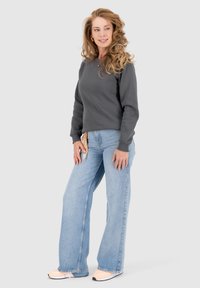 Grijze sweatshirt met lange mouwen, gecombineerd met lichtblauwe wijde jeans. De outfit wordt aangevuld met lichtgekleurde sneakers.