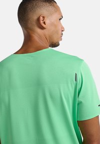 Camisa atlética verde con un diseño de malla texturizada y pequeñas perforaciones. Incluye detalles de acento en negro cerca de las costuras de los hombros.