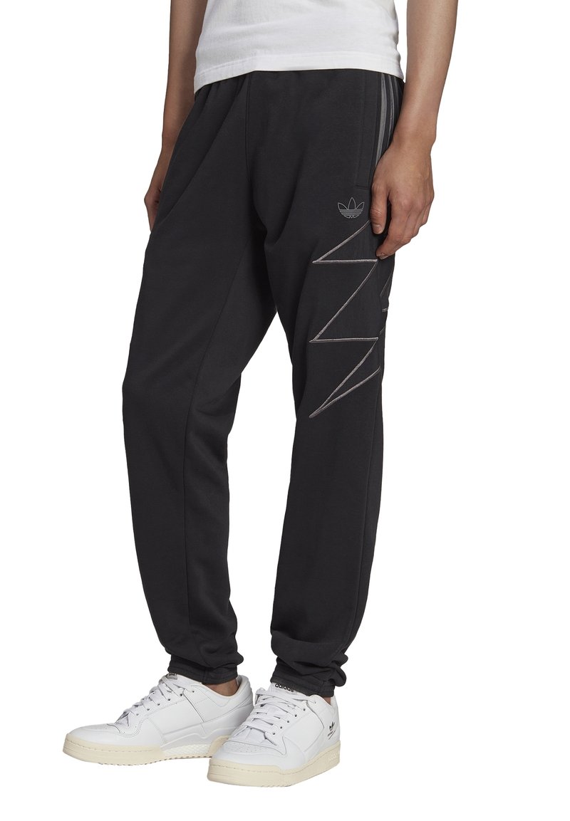 Černé tepláky s elastickými manžetami, dvěma bočními kapsami a tónovým zigzagovým vzorem na levé noze. Vyrobeny z měkkého, flexibilního materiálu.