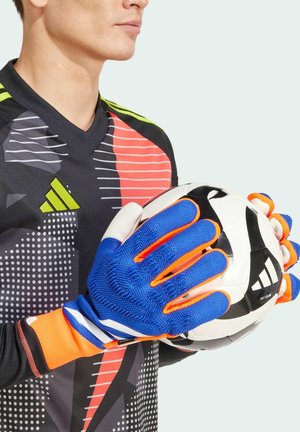 Gants de gardien de but avec des accents bleus et oranges, grip texturé et coupe ajustée, tenus avec un ballon de football noir et blanc contre un maillot à motifs.