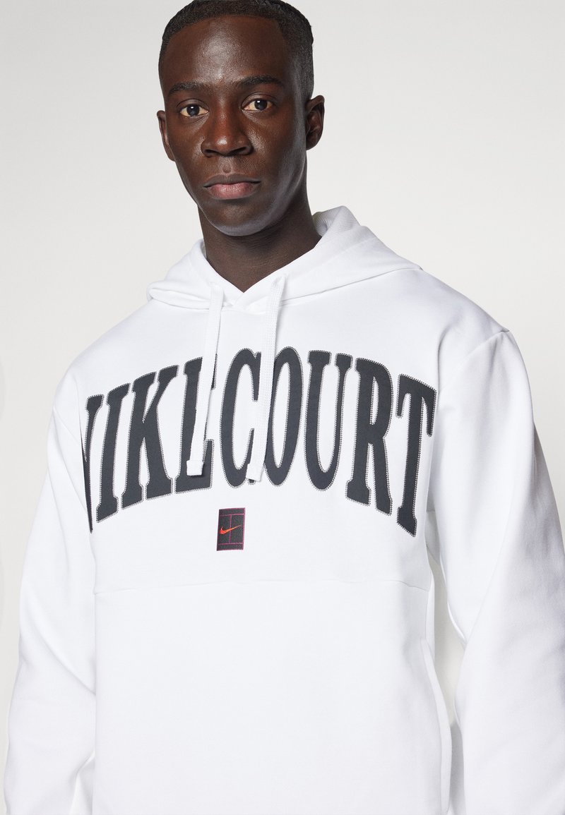 Sudadera blanca con capucha que presenta un gran texto negro "NIKELCOURT" en el pecho, con un pequeño detalle de logo rojo y negro. Textura de tela suave.