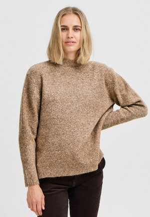 Maglione marrone a maglia con colletto alto, vestibilità ampia e maniche lunghe. Tessuto morbido e leggermente melangiato, abbinato a pantaloni scuri.