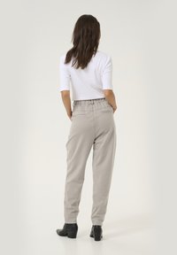 Pantalons gris clair, fuselés, avec une taille élastique, des poches latérales et une texture lisse, associés à un haut blanc ajusté.