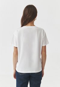 Hvid kortærmet t-shirt med afslappet pasform, rund halsudskæring og glat tekstur, båret med blå denim jeans.
