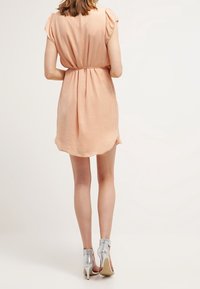Vestido de color melocotón con mangas cortas, cintura elástica y bajo redondeado. Combinado con zapatos de tacón alto plateados, mostrando una silueta elegante.