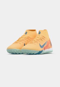 Pár oranžových vysokých sportovních bot Nike s modrým logem swoosh a mintově zelenou texturovanou podrážkou na bílém pozadí.