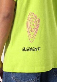 Neon grønn bomull T-skjorte med et rosa grafisk emblem og svart tekst "ELEMENT" nederst, med en avslappet passform og korte ermer.