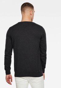 Pull noir à manches longues et col rond, doté d'un design en tricot texturé. Présenté de dos avec un ourlet uni.